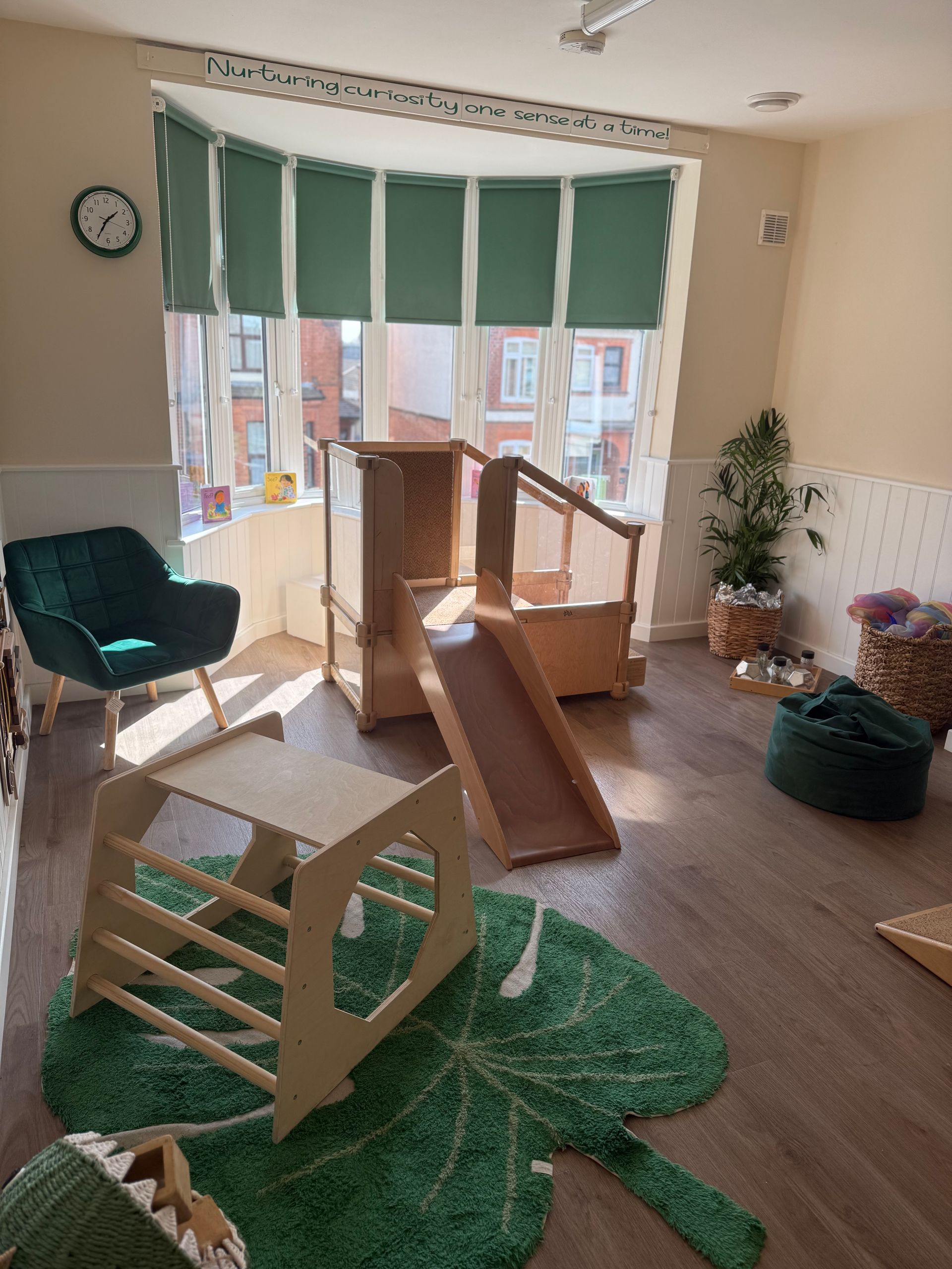 Bright playroom with wooden climbing toys, green cushions, and sunlight through windows