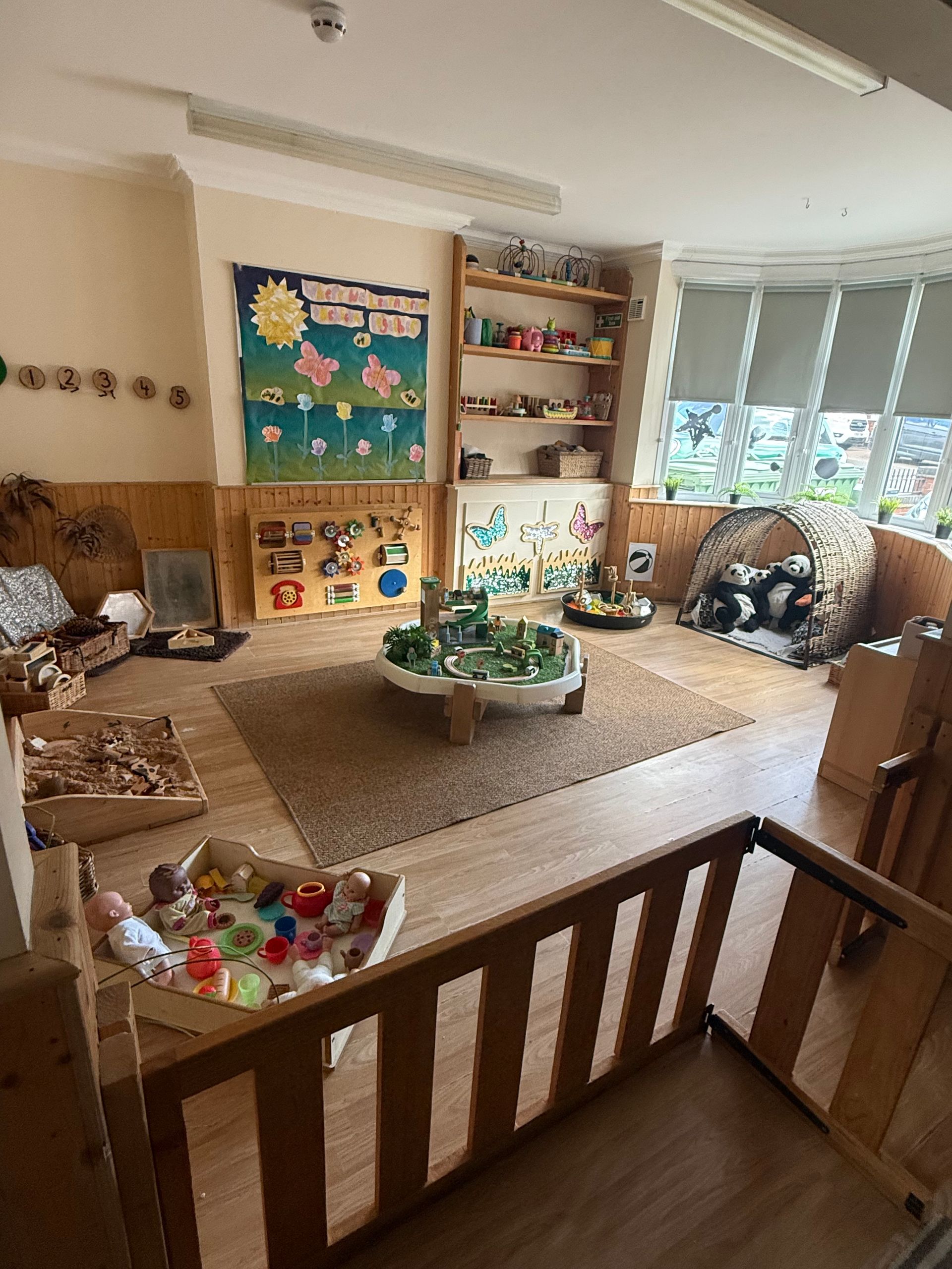 Classroom play area with toys, shelves, rugs, and a small table in a bright corner room