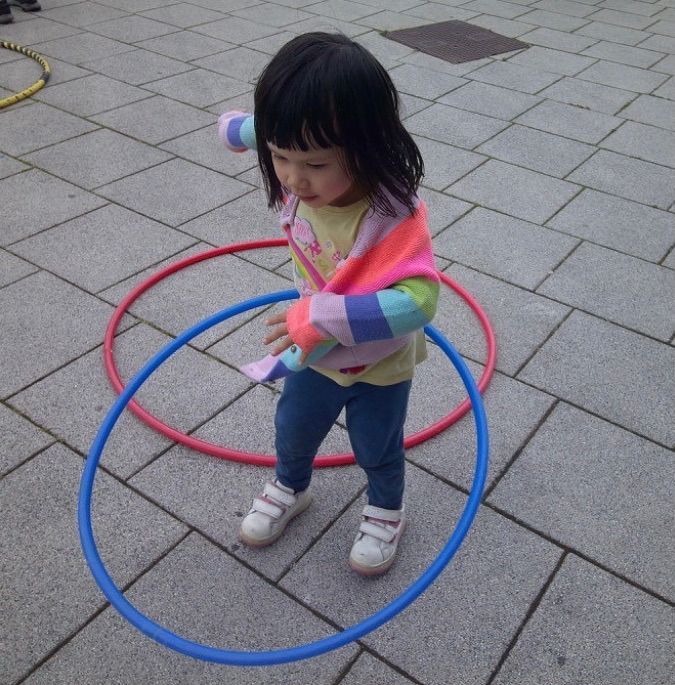 Child standing inside colorful hula hoops on a paved playground.