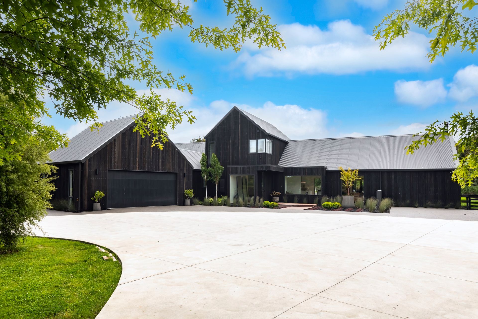 A large black barn shaped house with a driveway in front of it.