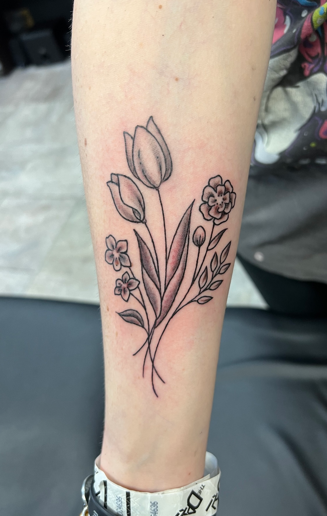 Tattoo of a floral bouquet on a person's forearm. Features tulips, small flowers, and leaves with shaded details.
