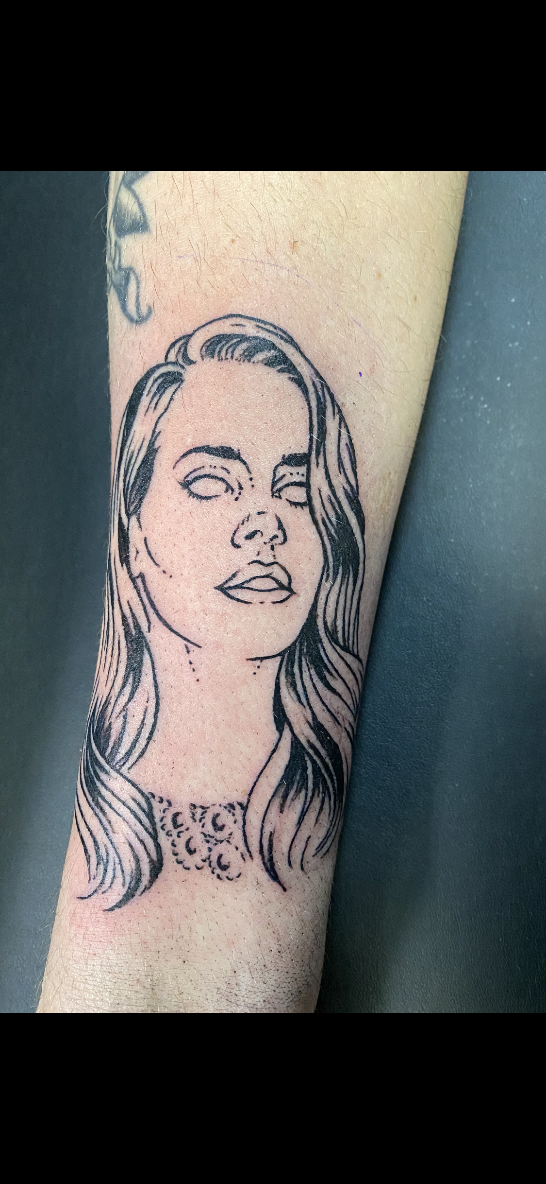 Tattoo of a woman's face on a forearm; black ink, lined style. Her eyes are blank.