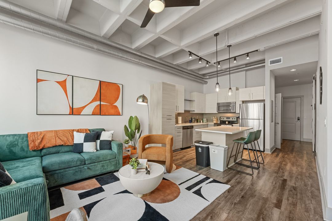 Modern open-concept apartment living room and kitchen featuring a green textured sofa, orange armchair, contemporary artwork