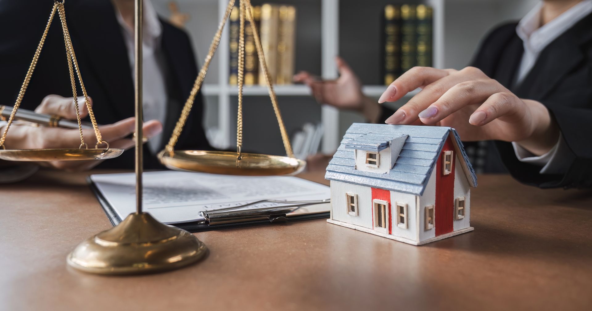 Legal professionals with scales, paperwork, and model house on table, likely discussing property.