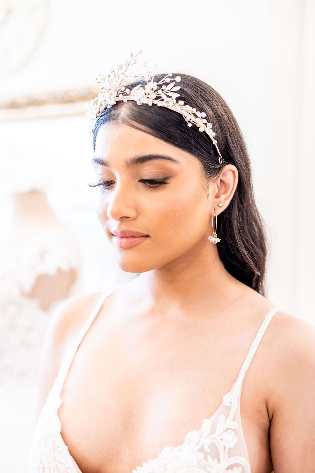 Woman wearing a bridal headband and earrings, looking down, in a light-filled room.