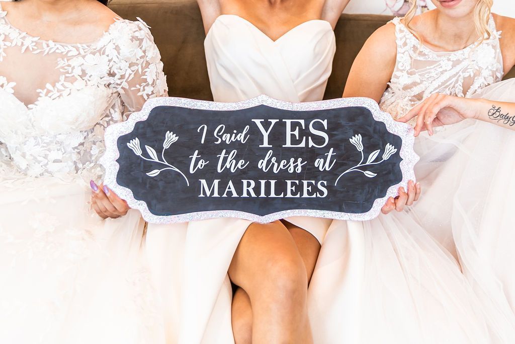 Three women in wedding dresses hold a sign that reads, 