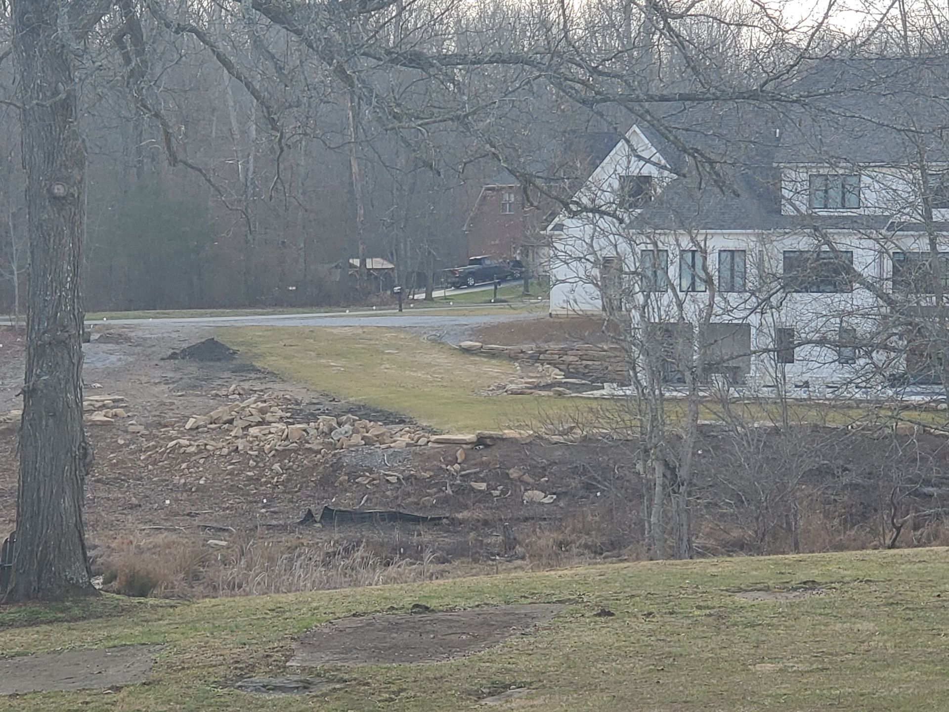 A large white house is sitting in the middle of a field surrounded by trees.