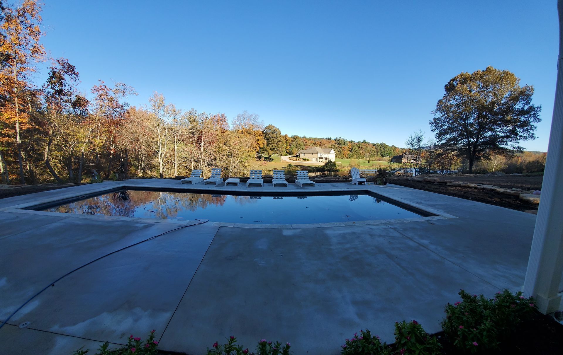 A large swimming pool surrounded by chairs and trees on a sunny day.