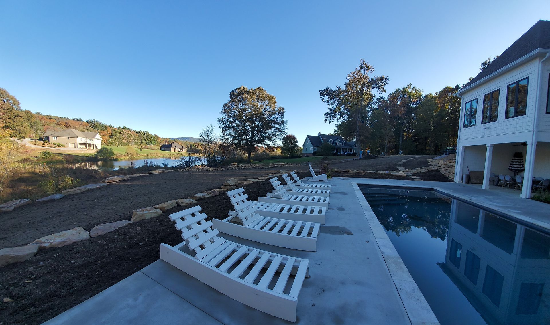 A row of white lounge chairs are lined up next to a large swimming pool.