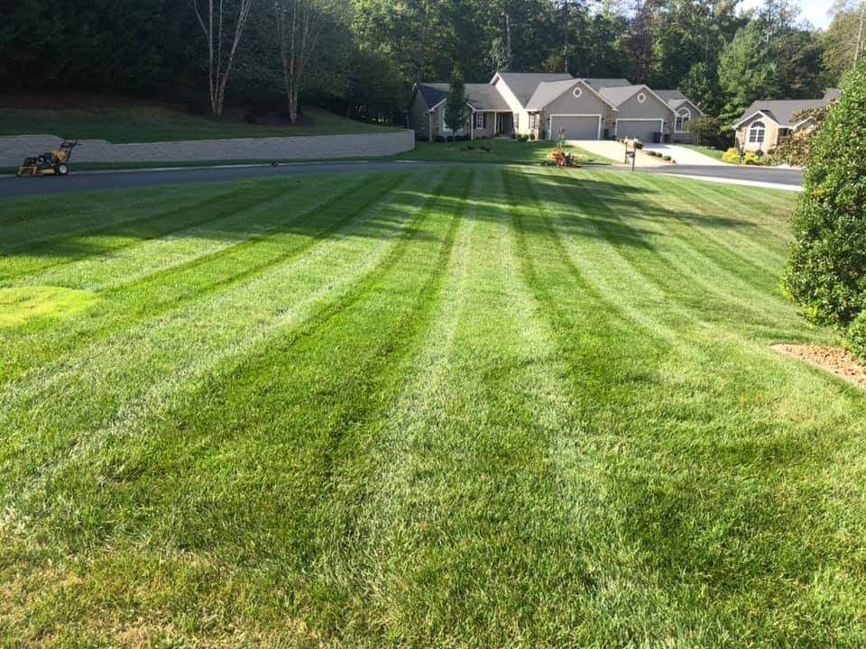 A lawn mower is cutting a lush green lawn in front of a house.