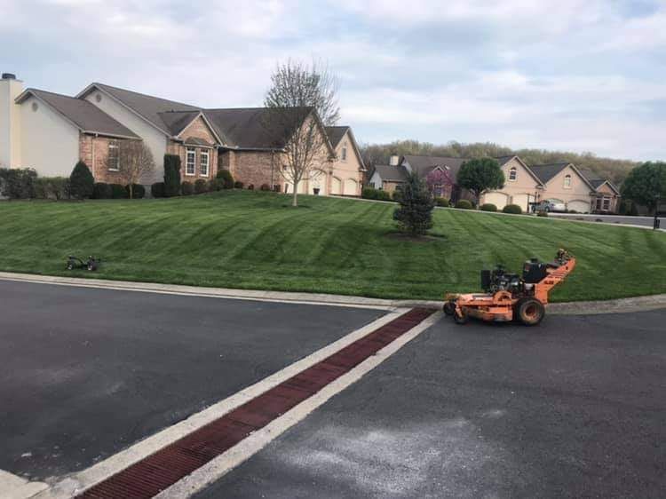 A lawn mower is cutting a lush green lawn in front of a house.