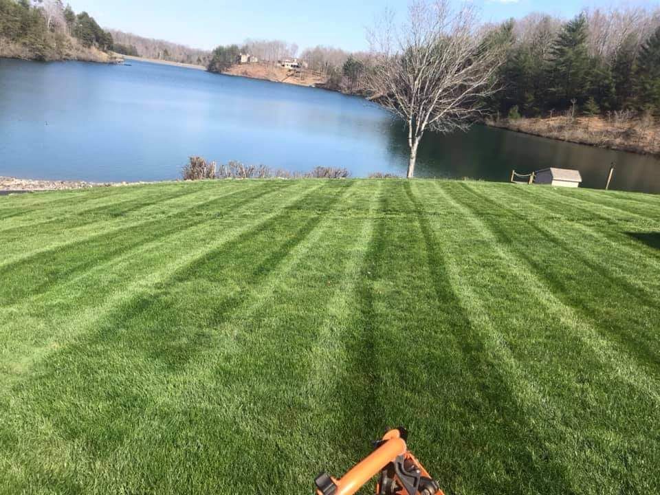 A lawn mower is sitting on top of a lush green lawn next to a lake.