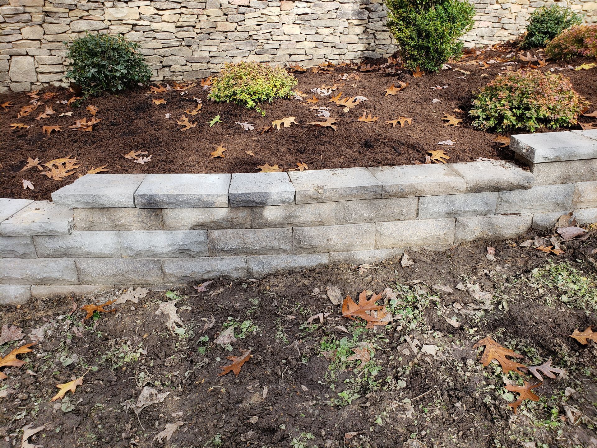 A stone wall is sitting in the middle of a garden.