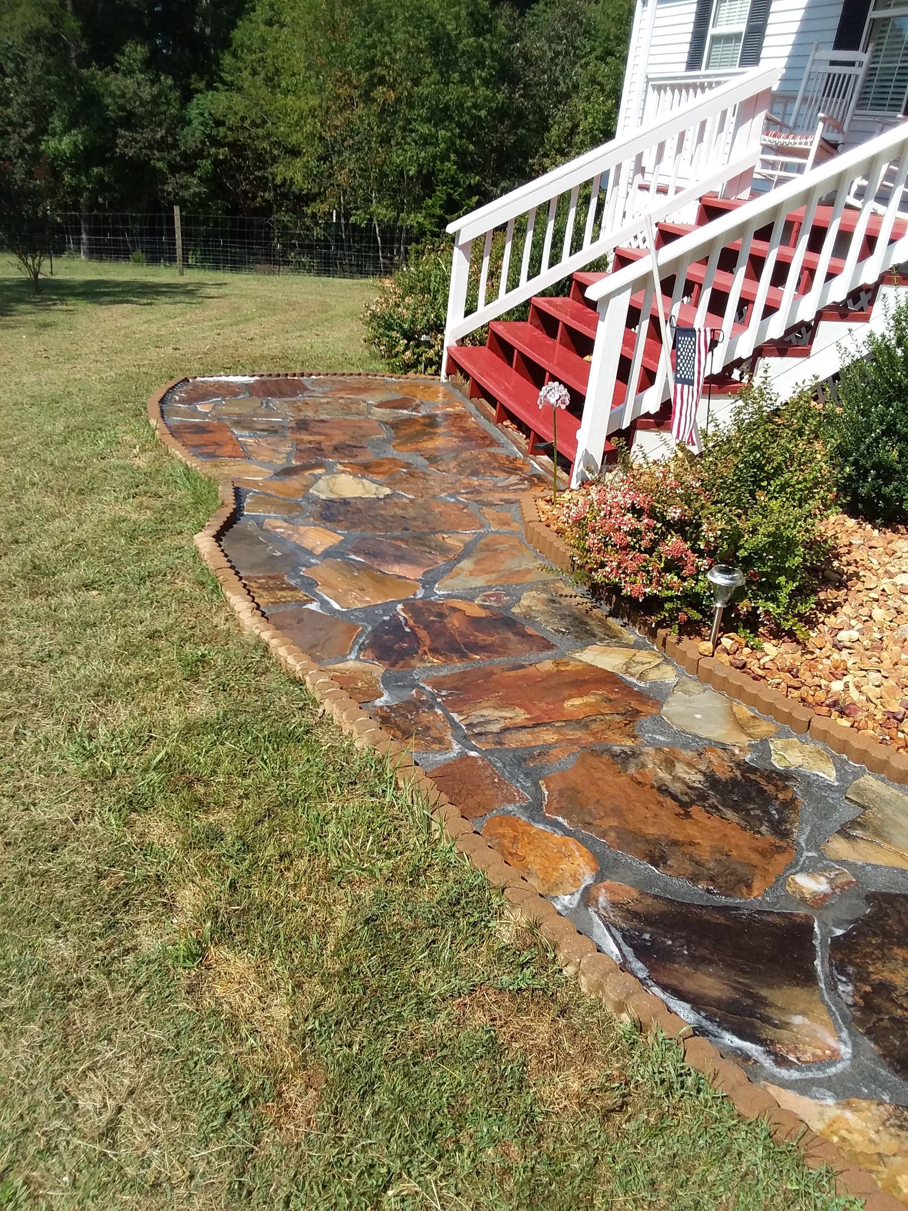 A stone walkway leading to a house with red stairs.