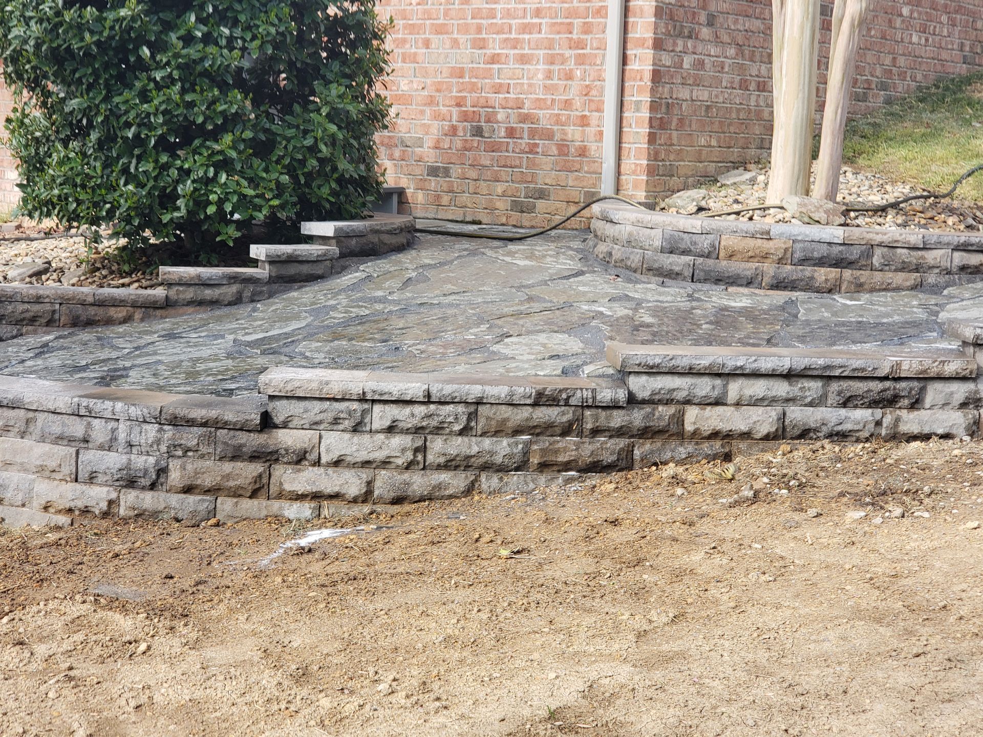 A brick wall with steps leading to a patio in front of a brick building.