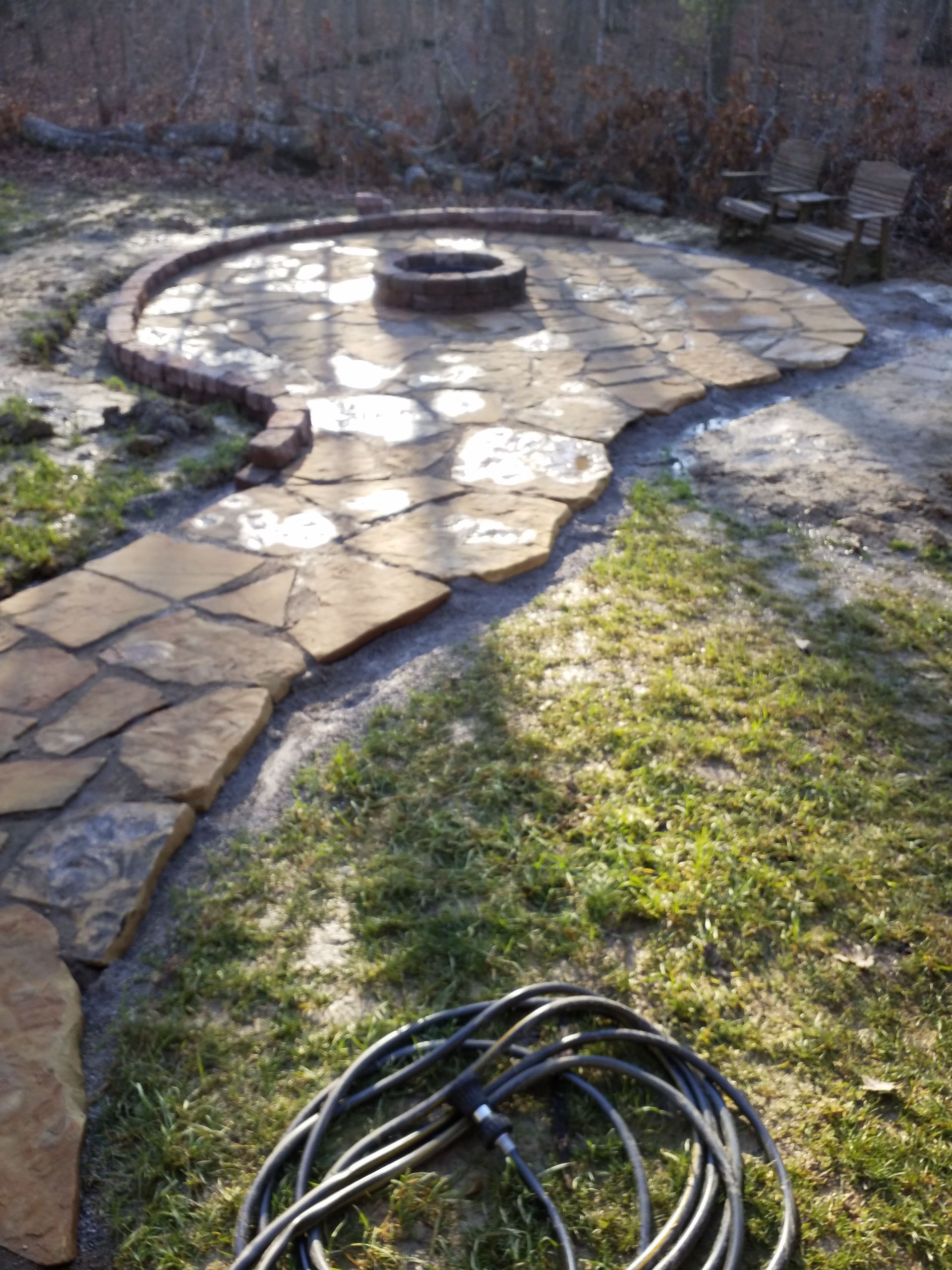A hose is sitting in the grass next to a fire pit.