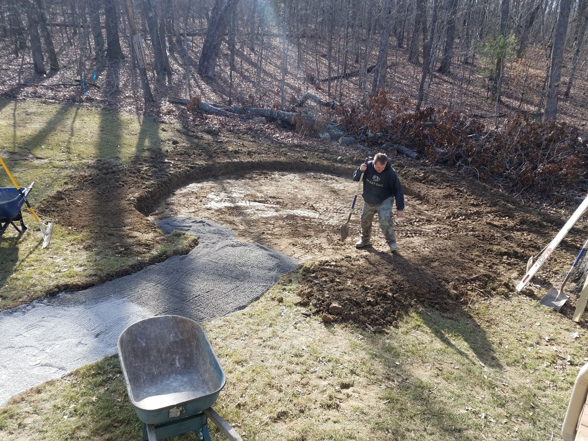 A man is standing in the dirt next to a wheelbarrow.