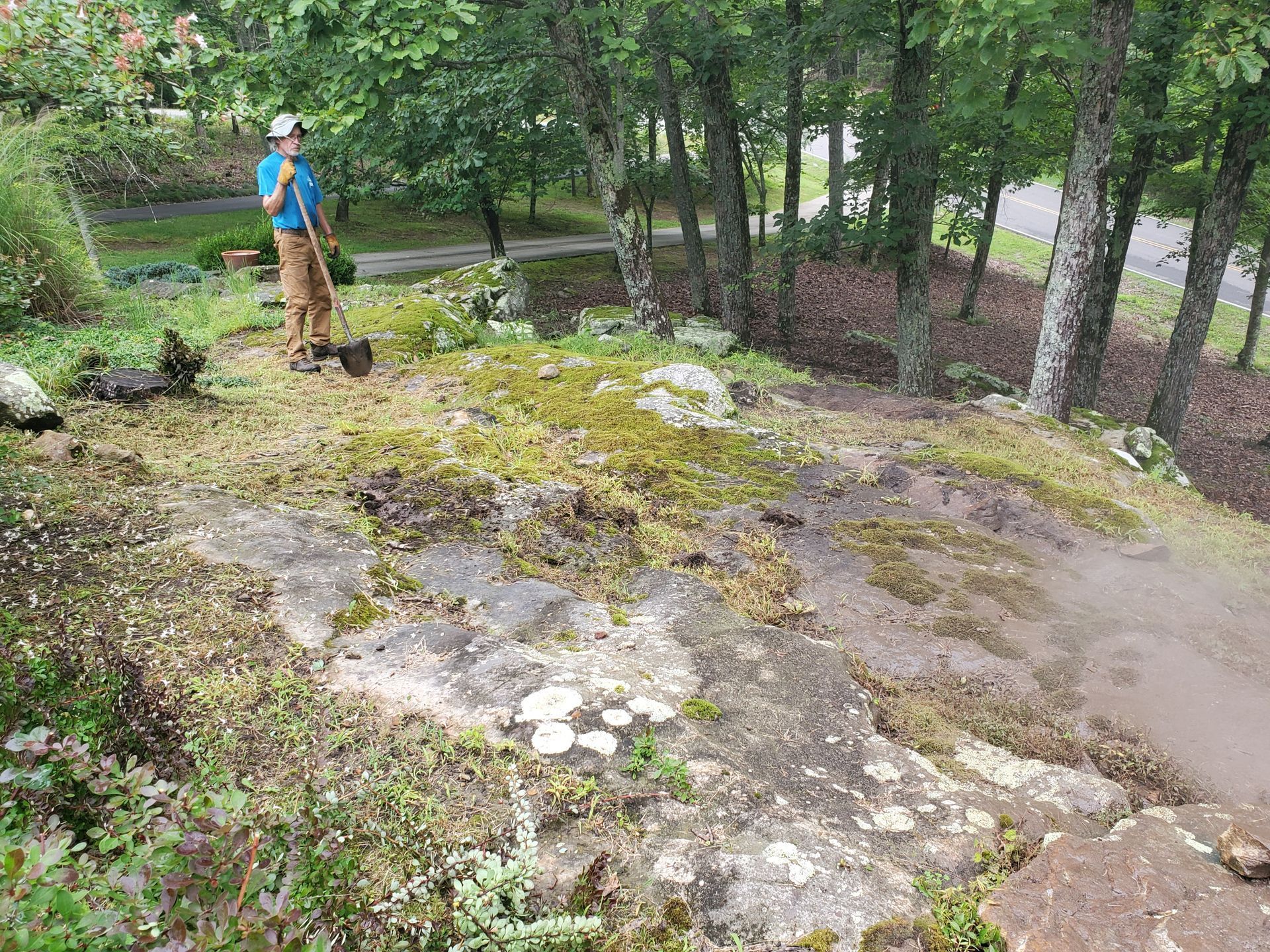 A man is standing on top of a rocky hill holding a shovel.