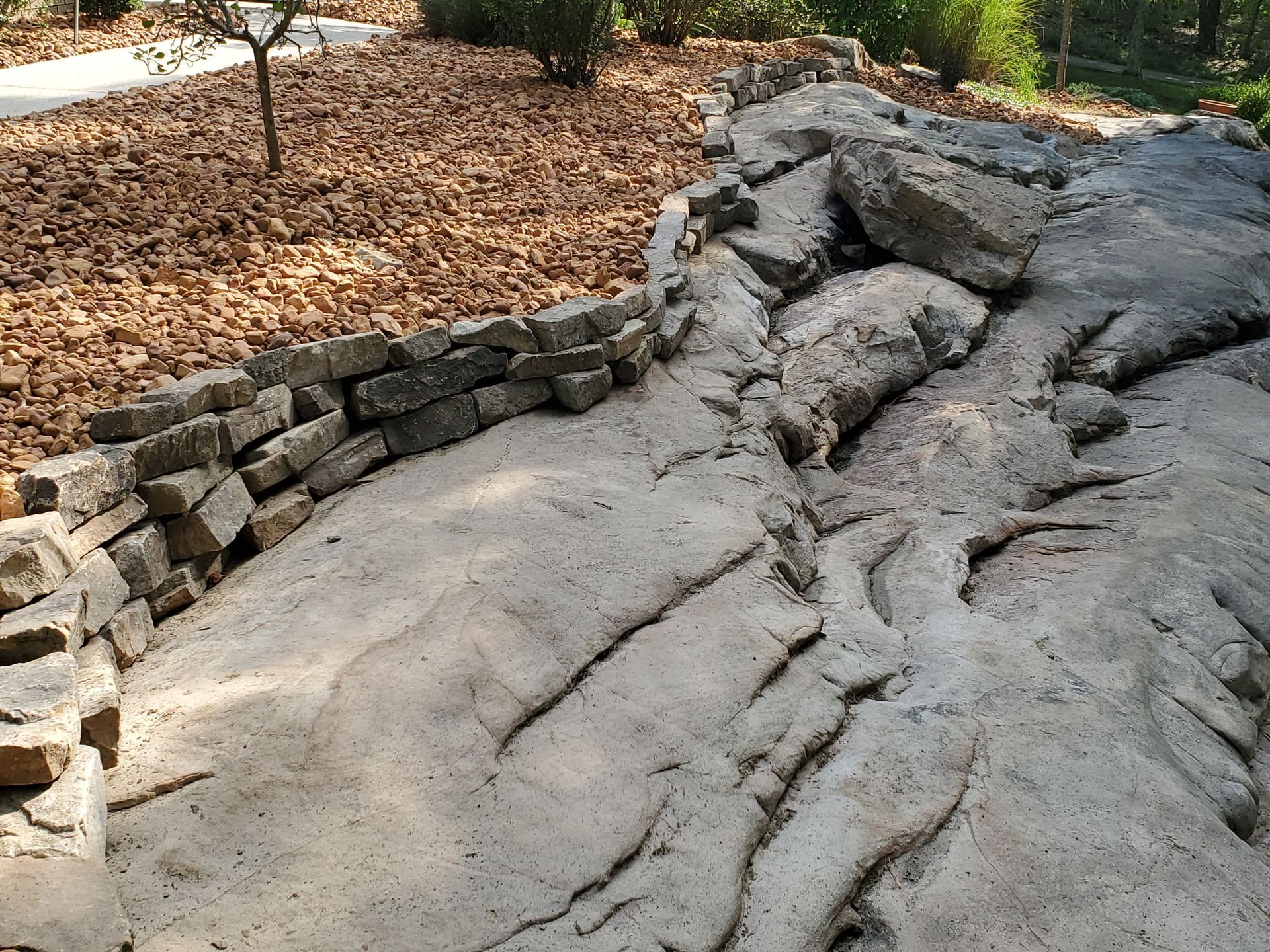 A large rock formation in the middle of a park surrounded by trees and leaves.