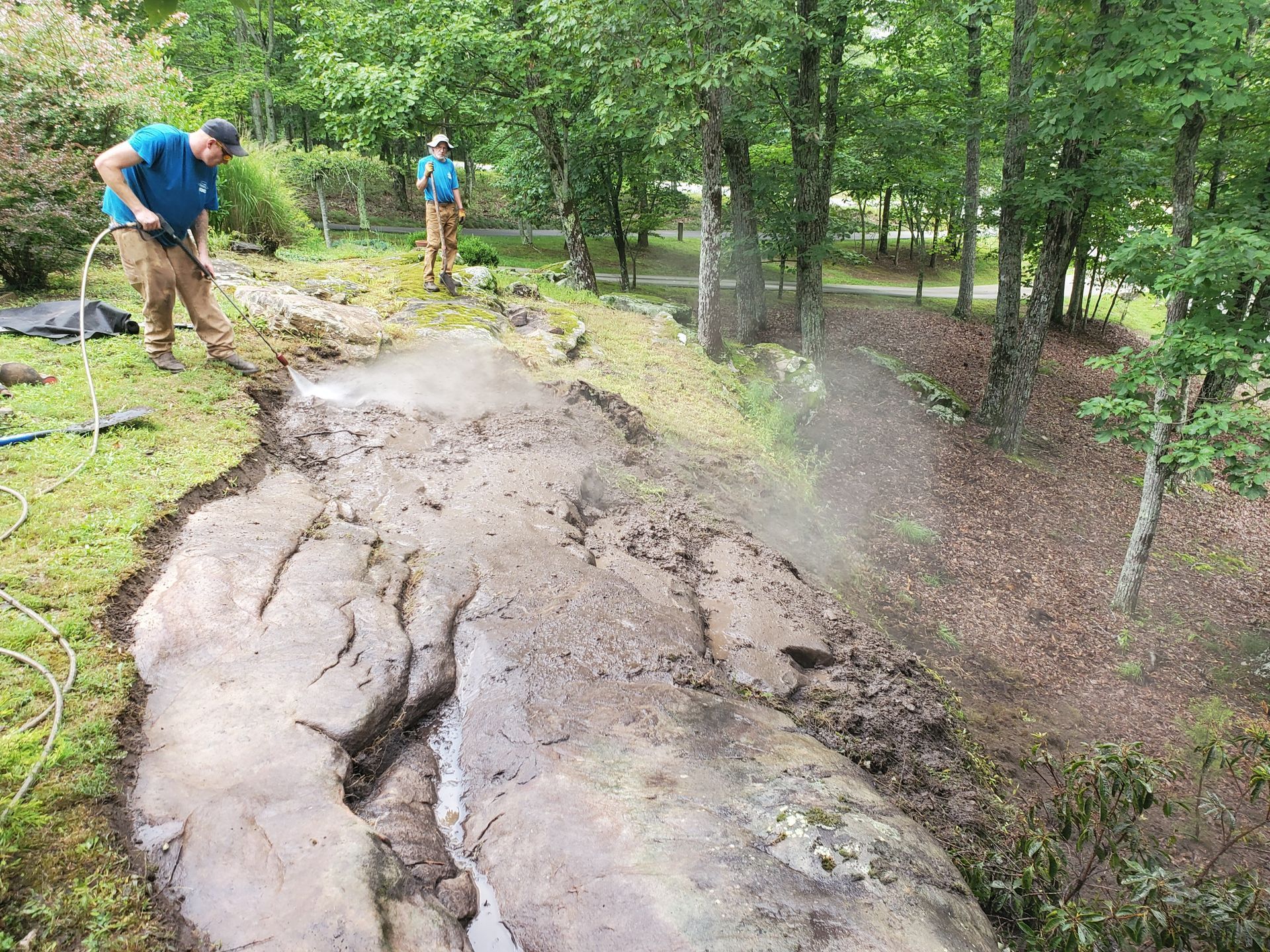Two men are working on a muddy path in the woods.