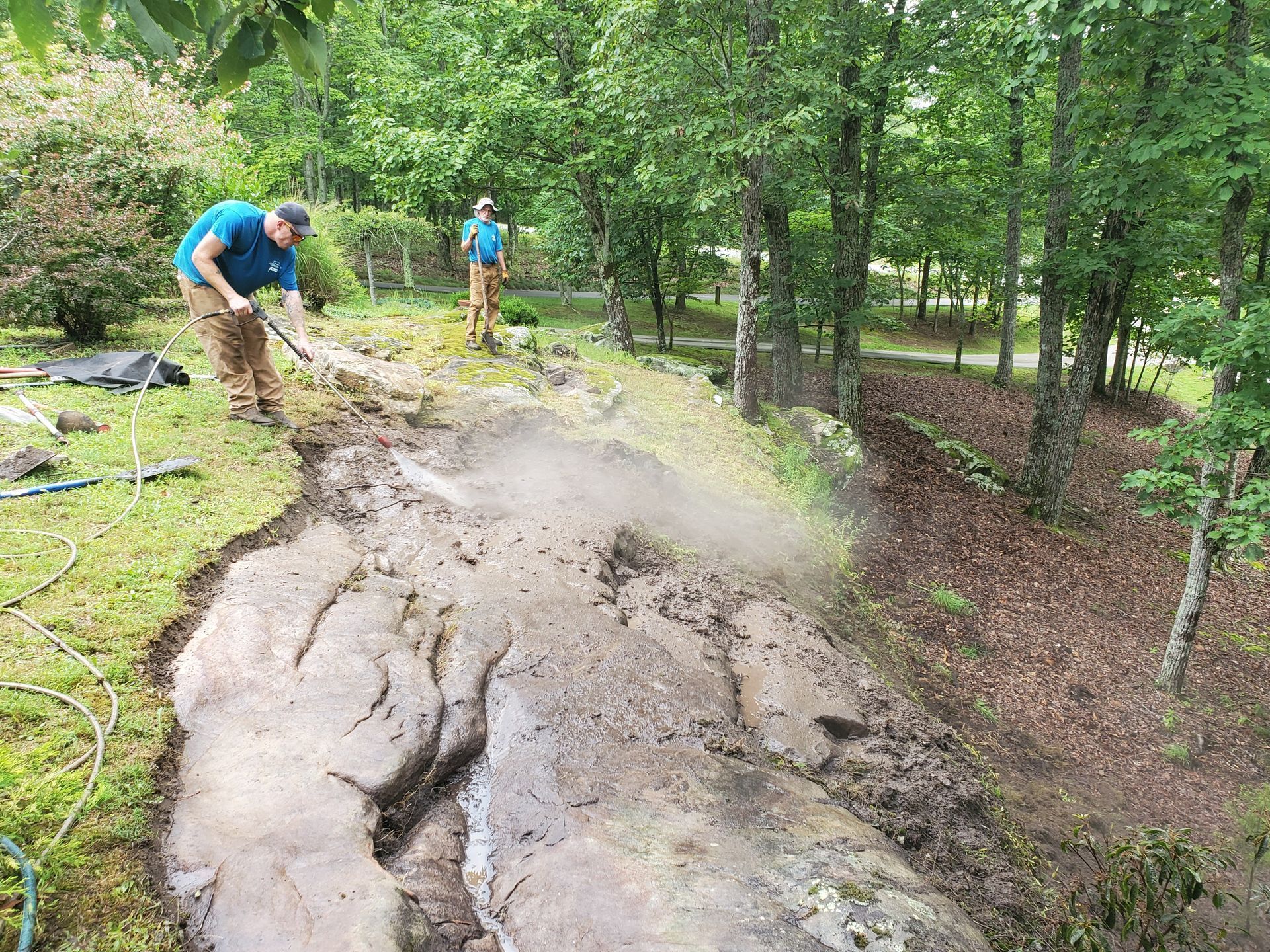 Two men are hosing off a rock in the woods.