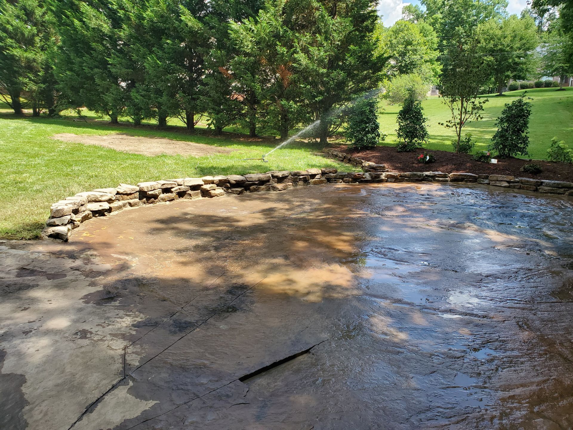 A sprinkler is spraying water on a muddy area in a park.