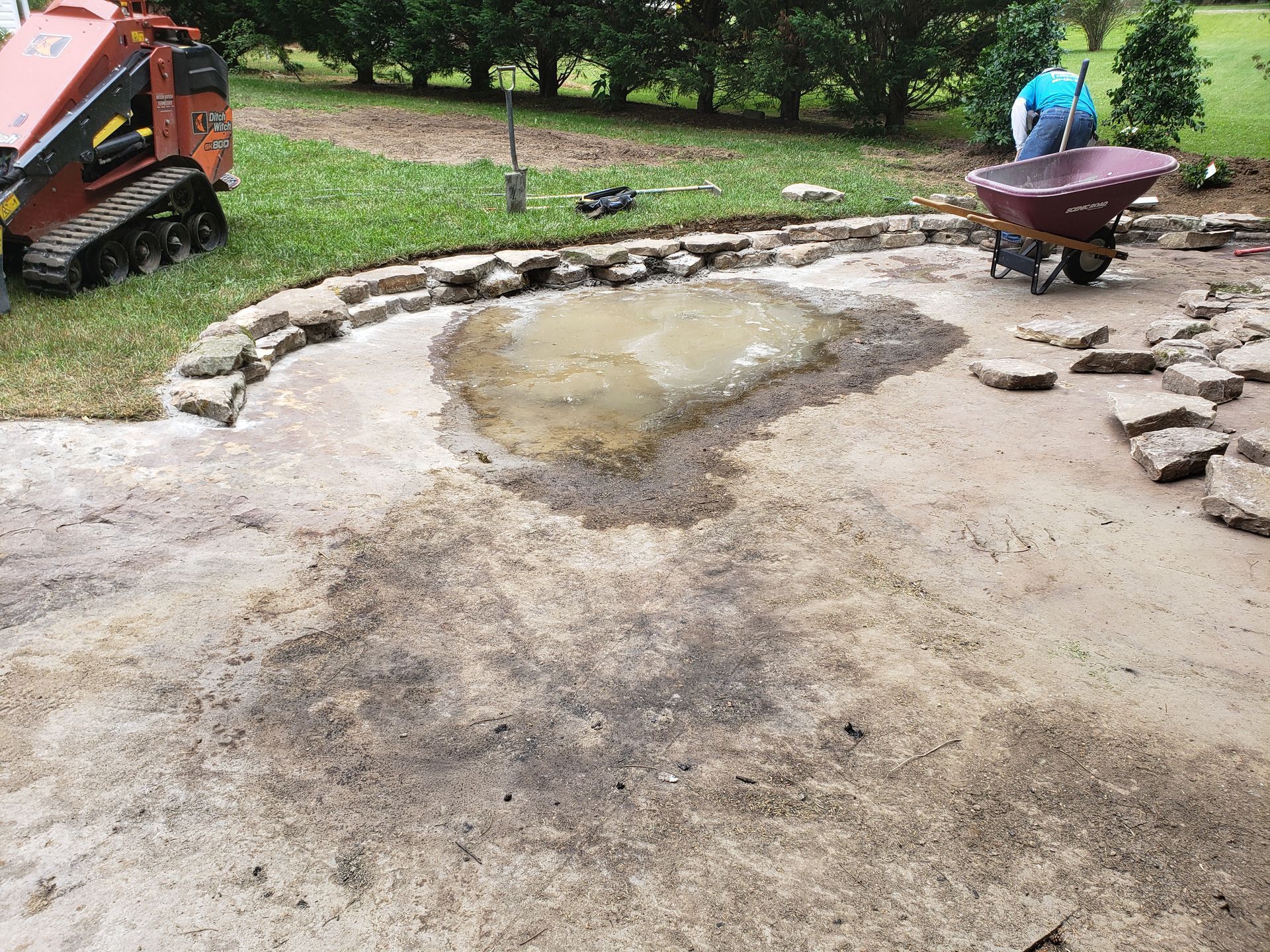 A man is using a wheelbarrow to move dirt on a patio.
