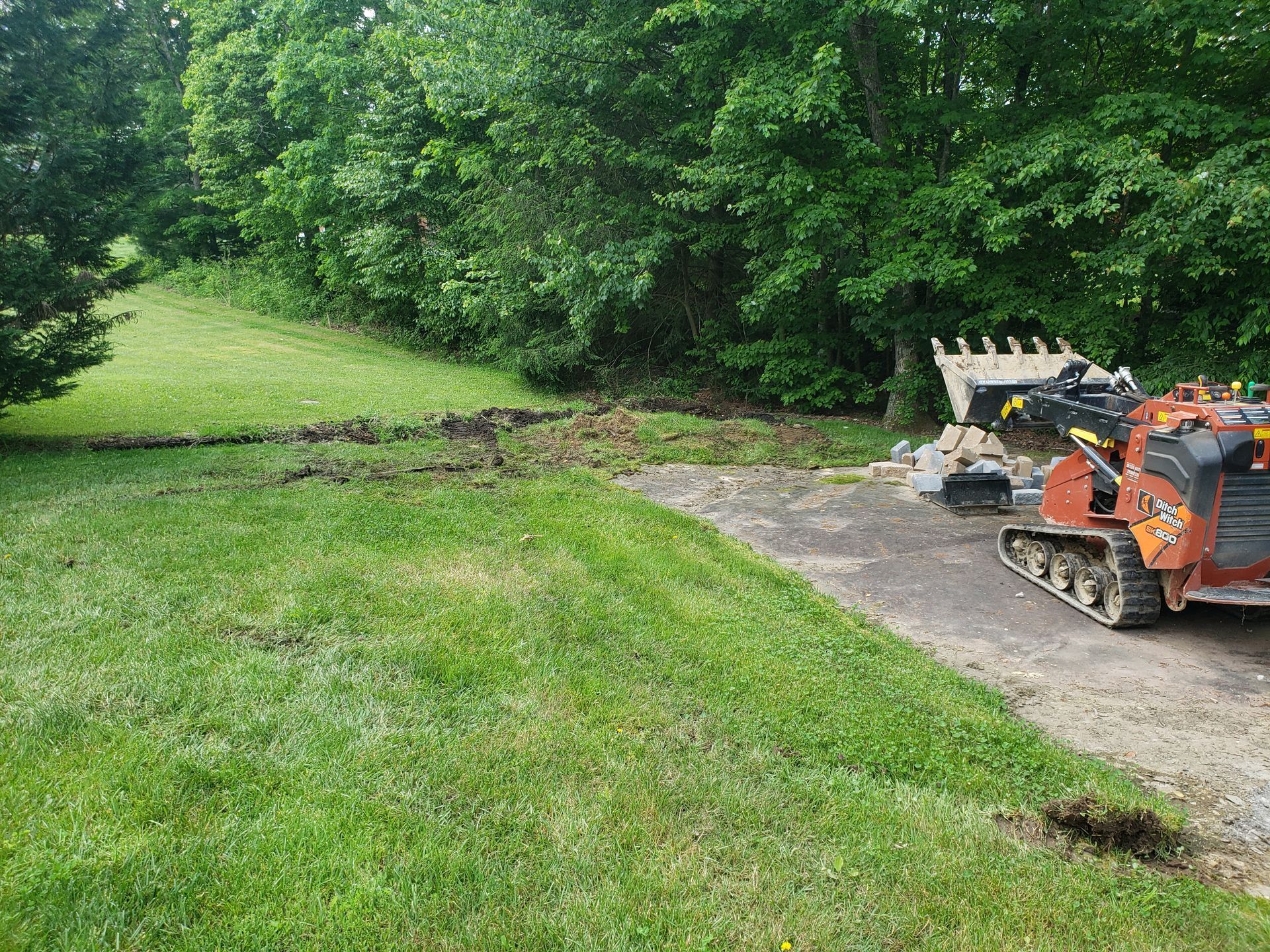 A bulldozer is parked in a driveway next to a lush green field.