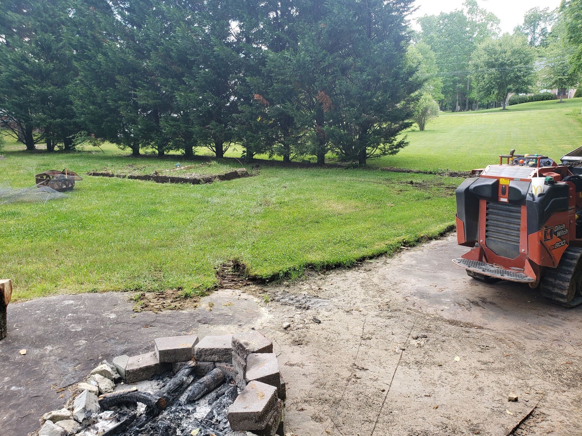 A tractor is parked in a driveway next to a fire pit.