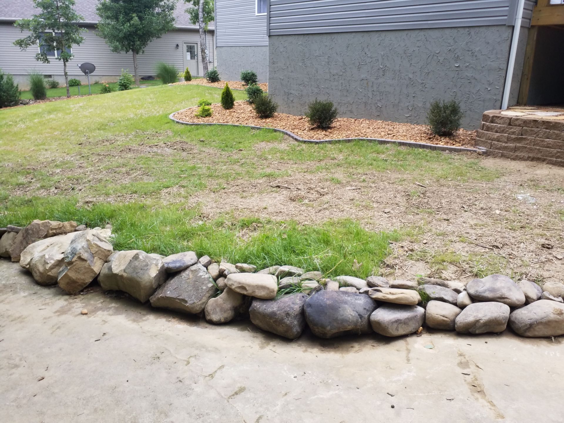 A rock wall surrounds a lush green lawn in front of a house.