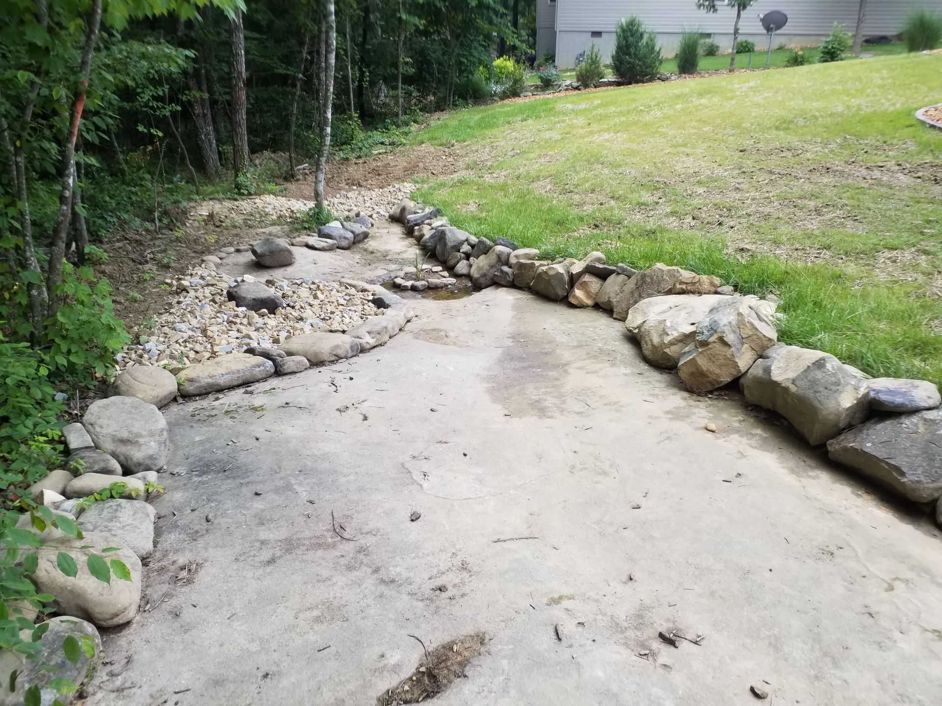 A concrete walkway surrounded by rocks leading to a grassy field.