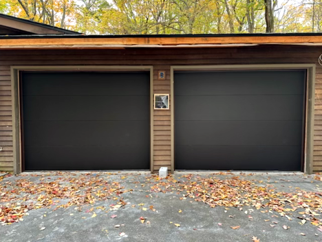 Two workers installing a new gray garage door in front of a house. One is on a ladder. Two workers installing a new gray garage door in front of a house. One is on a ladder.