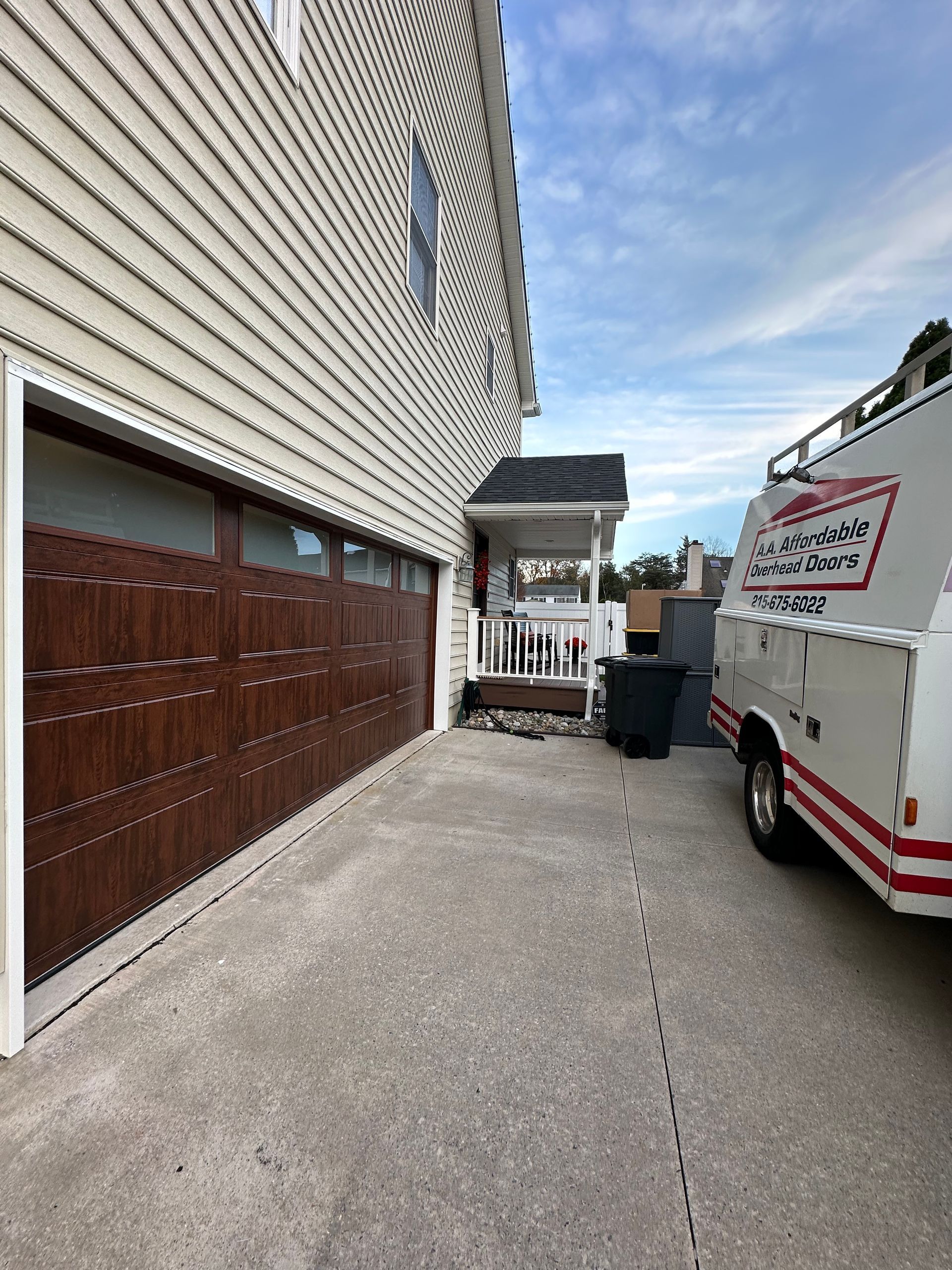 Two workers in blue coveralls installing a white garage door inside a garage.