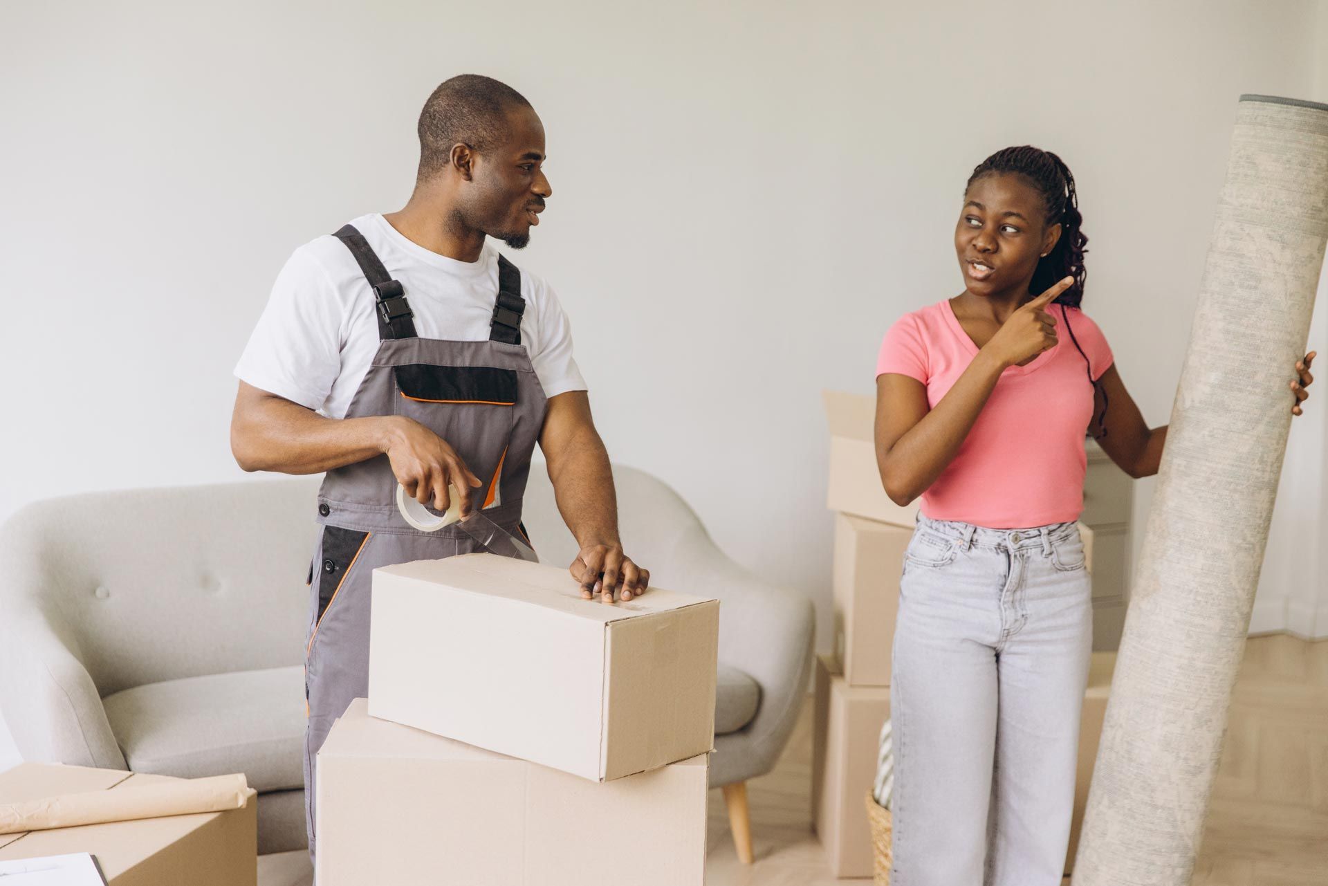 An African American mover packing next to a female African American client carrying a rolled carpet