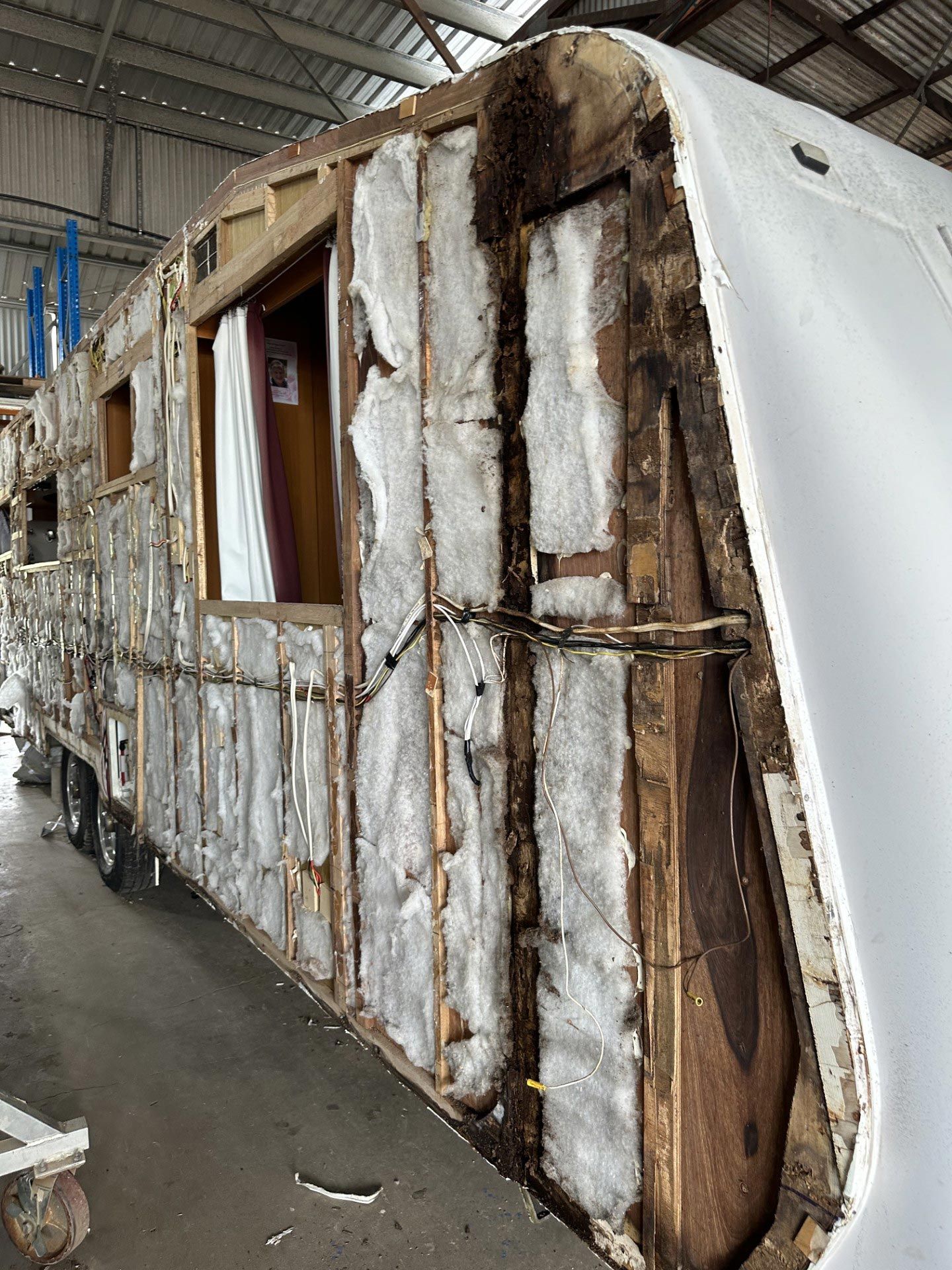 Damaged, stripped trailer body inside a warehouse, with exposed insulation and brown paneling