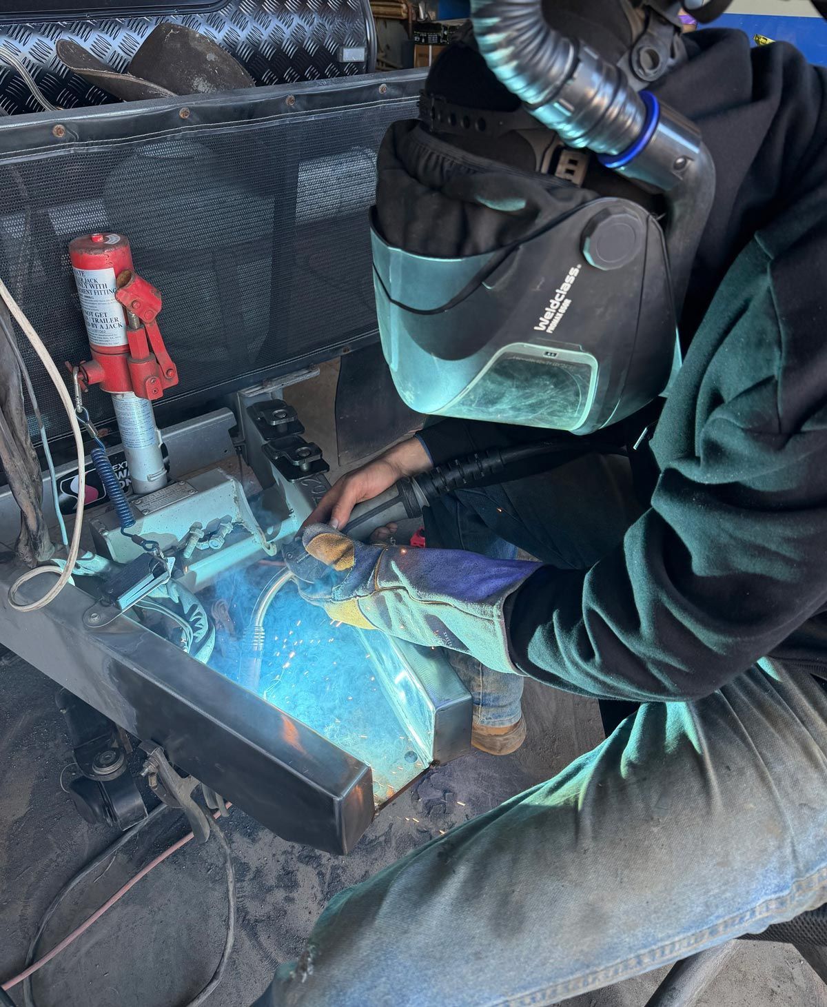 Person welding metal inside a vehicle cabin, bright blue sparks and protective gear visible