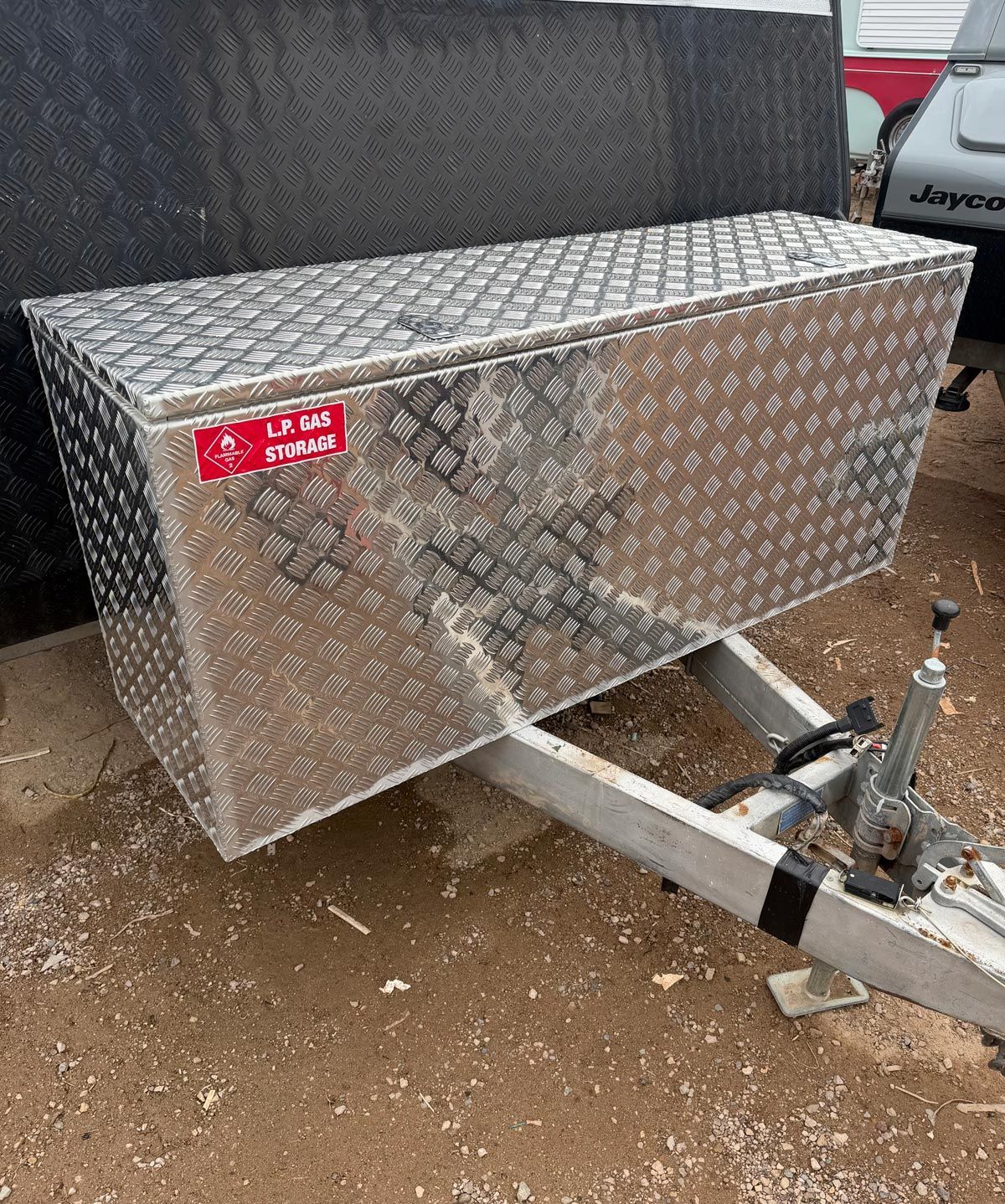 Silver diamond-plate trailer toolbox on a hitch in a muddy lot