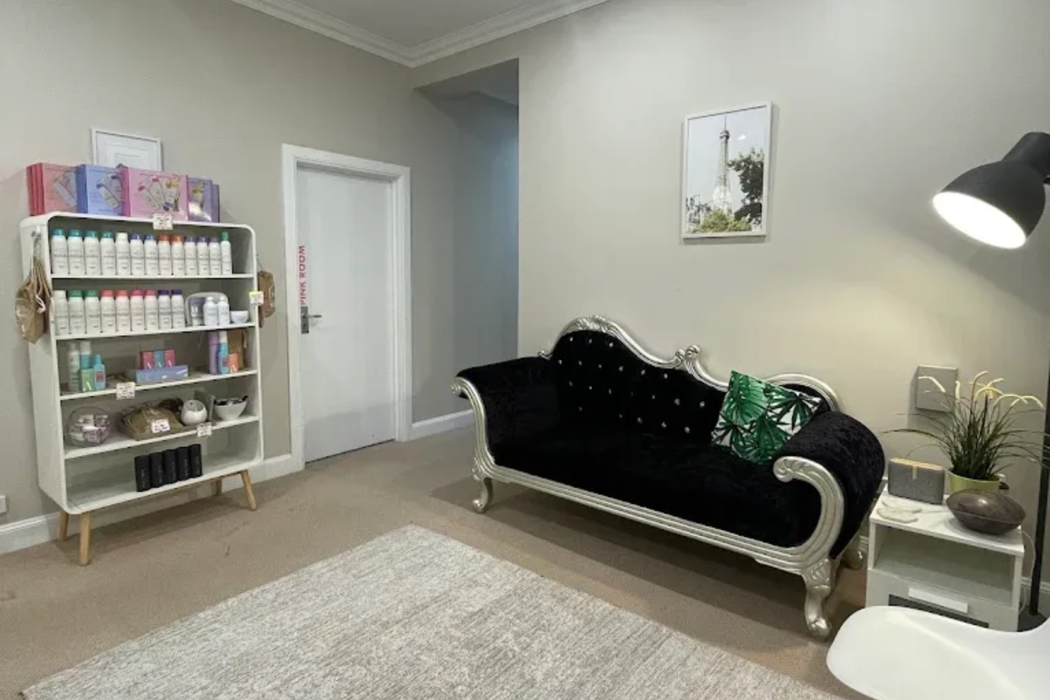 A beauty salon interior with a sofa, shelving, products, and a door, in neutral tones.