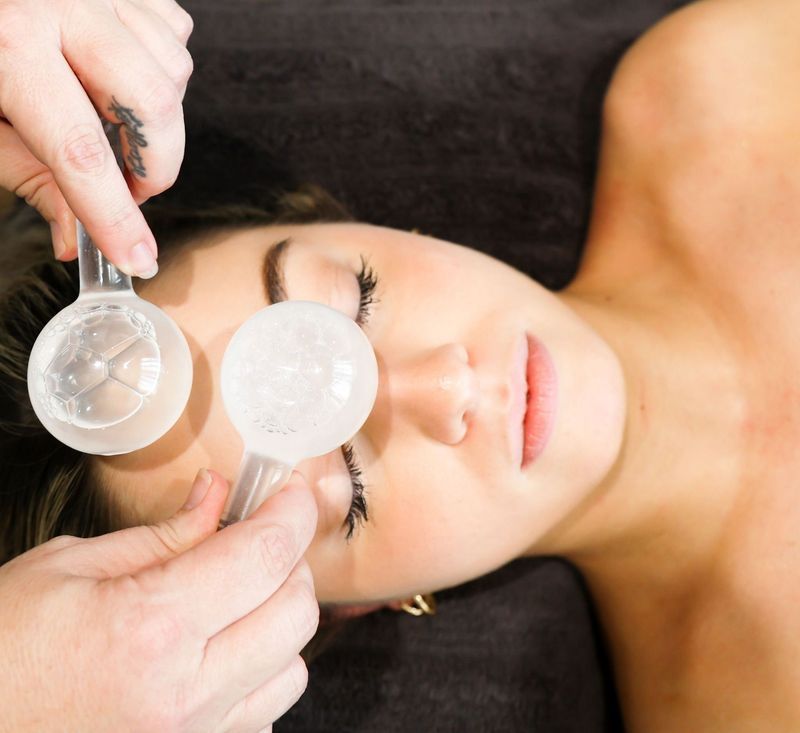 Woman receiving a facial treatment with cooling globes on her eyelids.