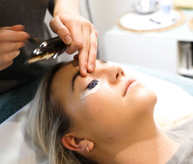 Person getting eyelash extensions applied; technician working with tweezers, eyes closed.