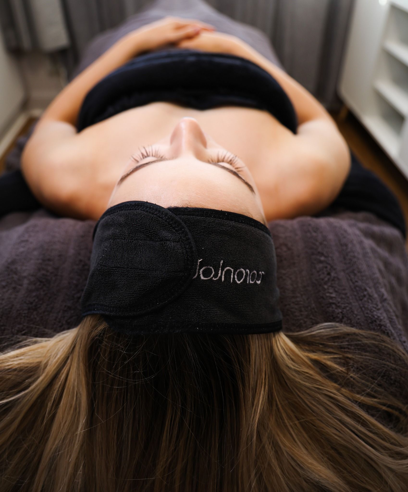 Person lying face up on massage table wearing a black headband with the word 