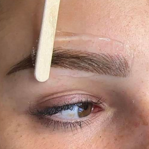 Waxing eyebrow with wooden spatula, close-up. Transparent wax on brow, eye visible.