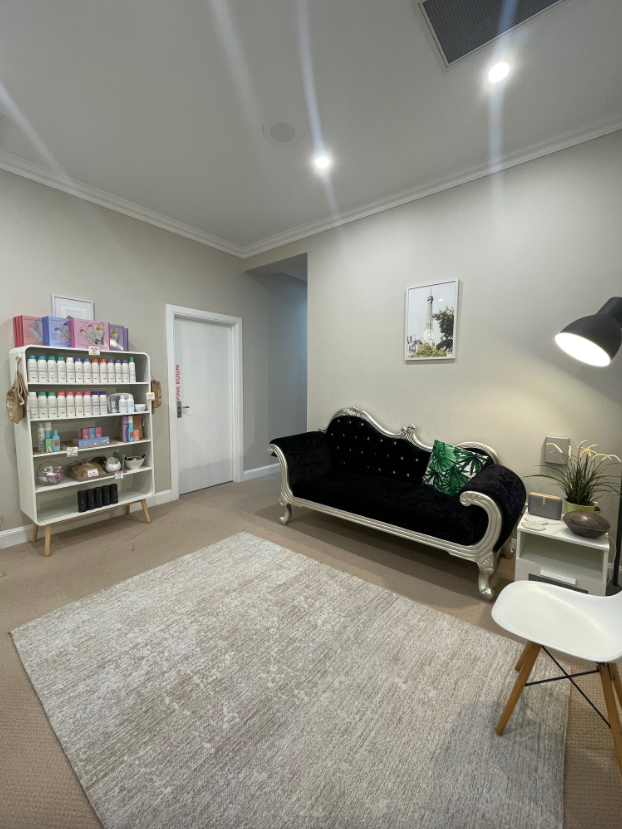 A waiting room with a chaise lounge, a shelf of products, and a rug.