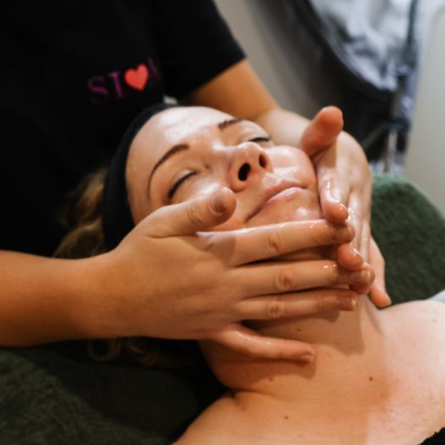 Woman receiving facial massage with closed eyes, hands applying product.