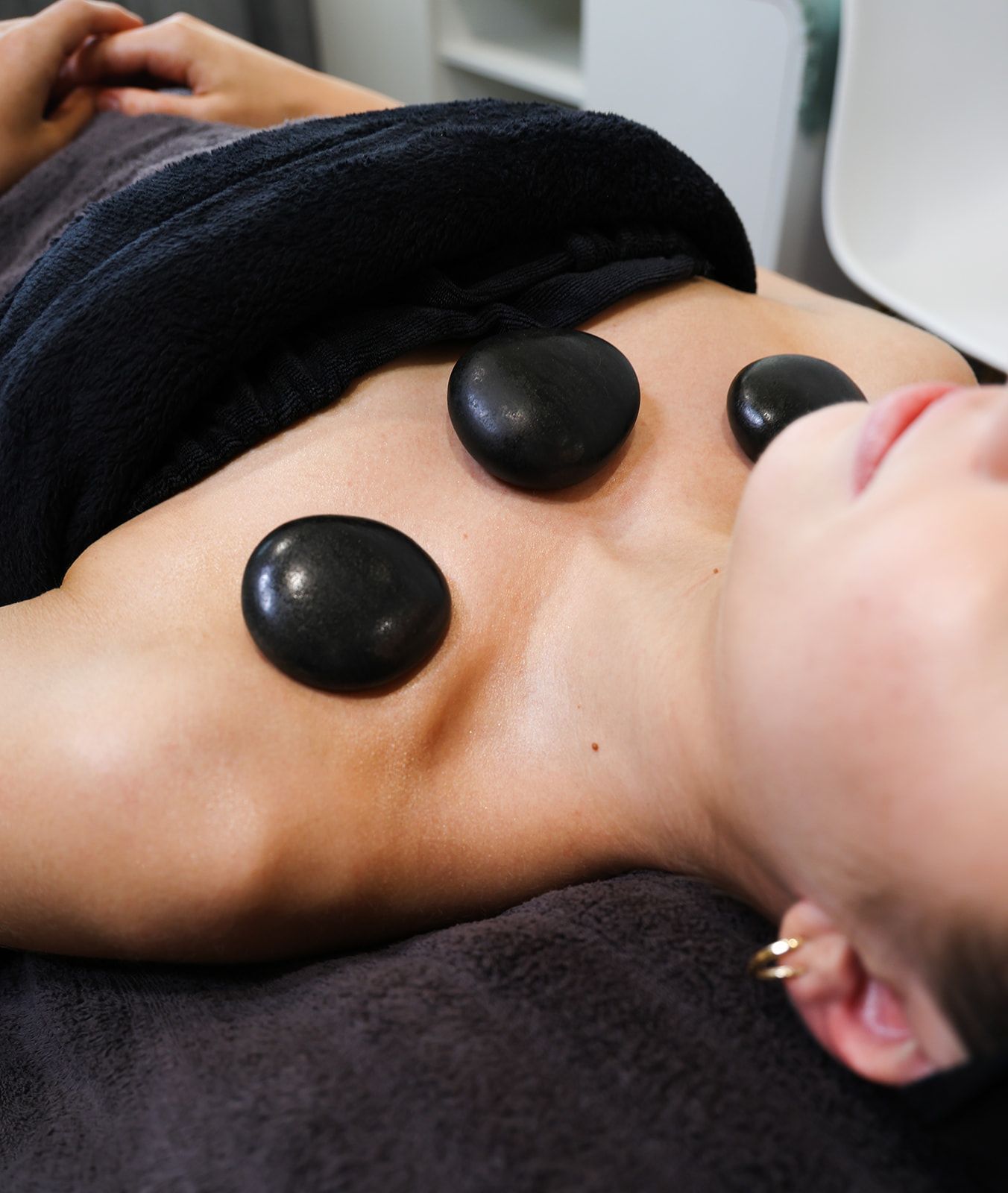 Person receiving hot stone massage on chest, with black stones and black towel.