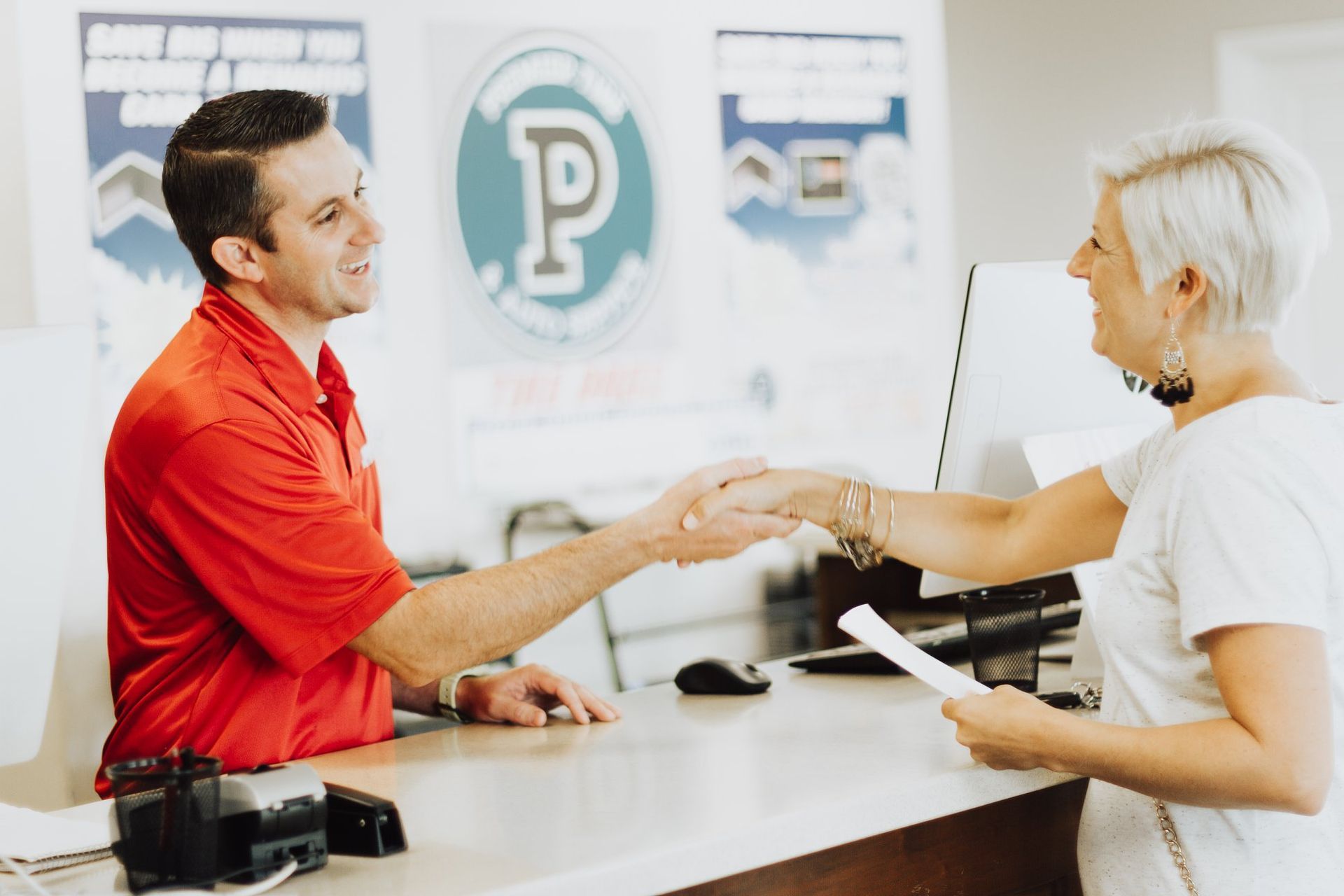 A man in a red shirt is shaking hands with a woman in a white shirt.