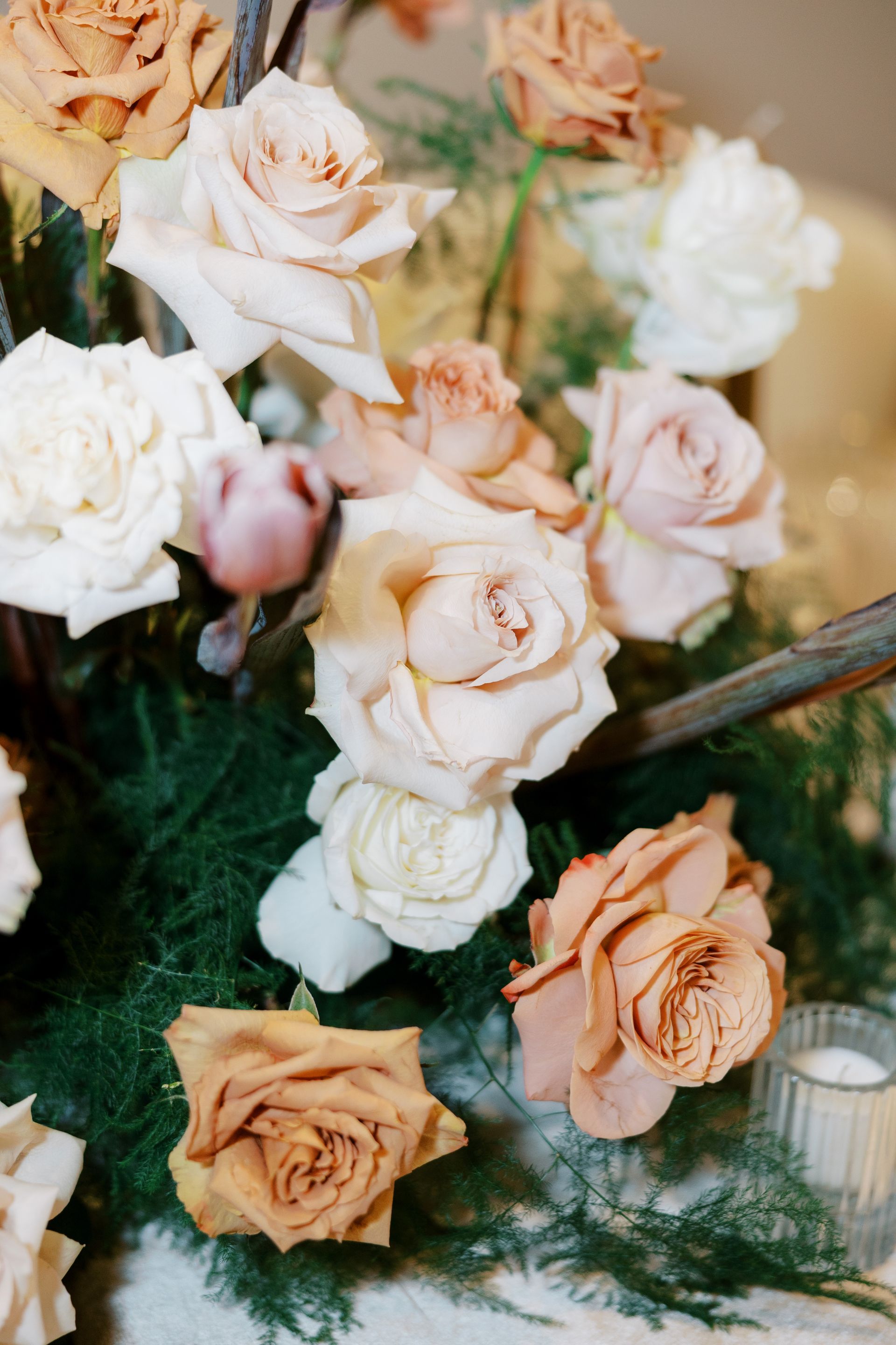 Close-up of a floral arrangement with peach, cream, and white roses, set among green foliage.