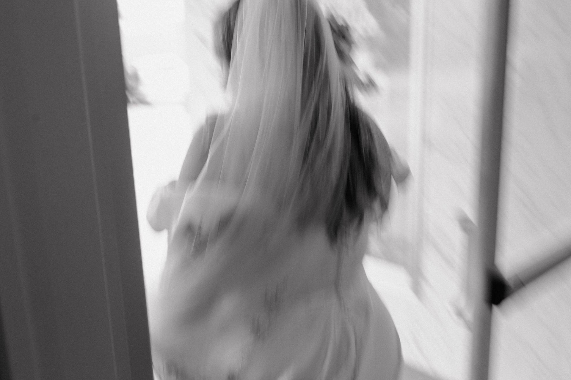 Dog running through an open doorway, seen from behind. Black and white.