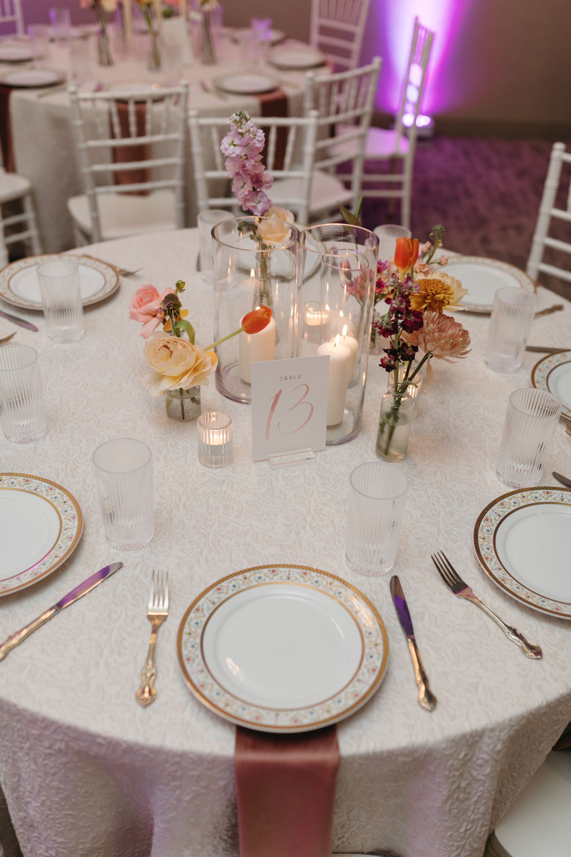 Round table set for a wedding, with floral centerpieces and formal place settings; white and gold accents.