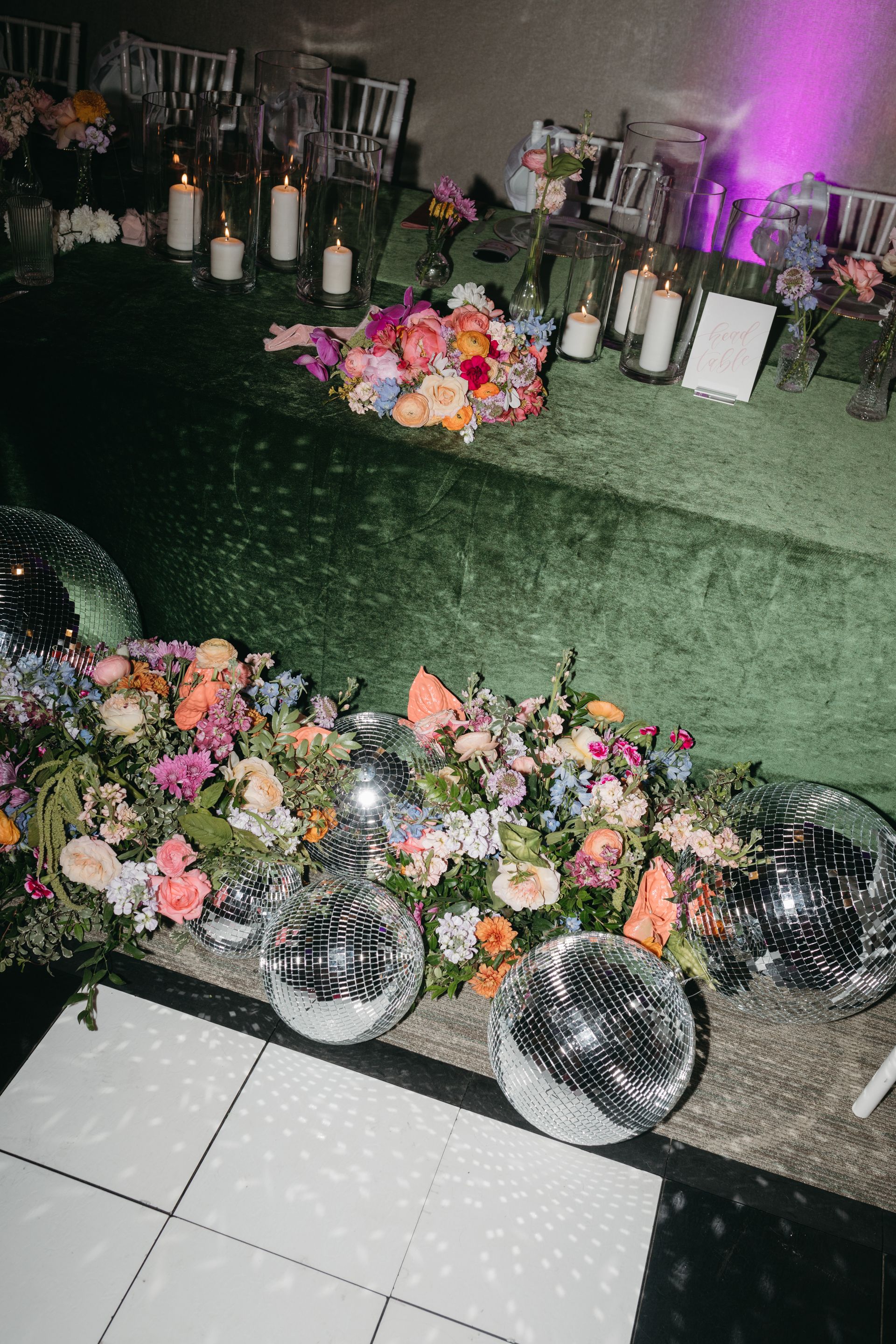 Table with floral arrangements, disco balls, and candles; wedding reception setting.
